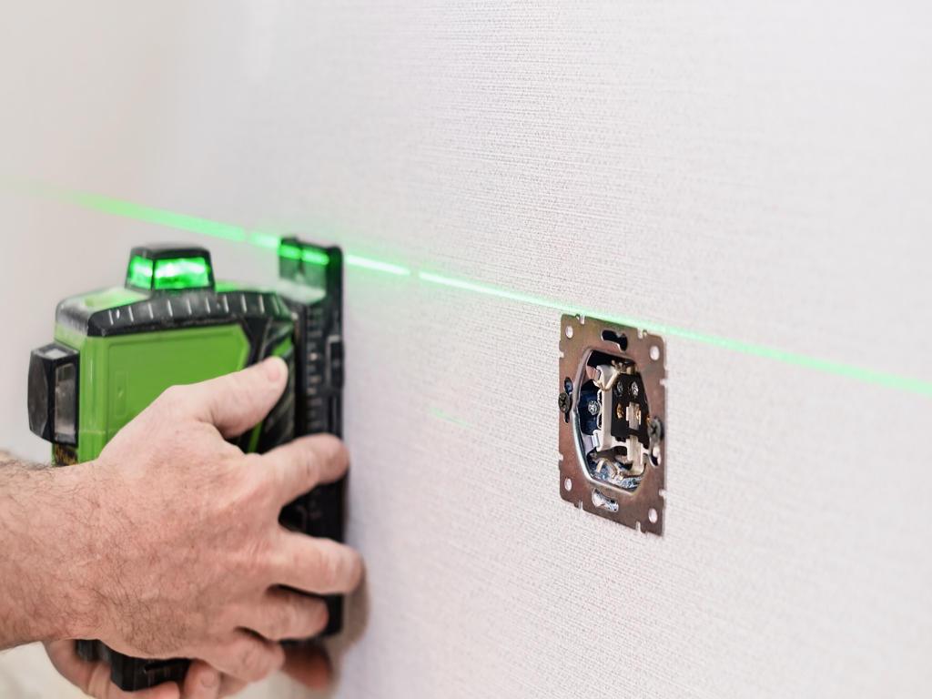 An electrician installs sockets in the apartment. Checking the installed sockets on the wall of the apartment with a laser level, selective focus on the sockets